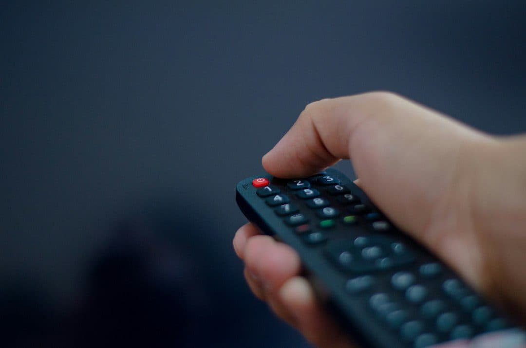 A hand pressing the buttons of a TV remote in a dark room, as when setting up NEWDYTV on a Firestick