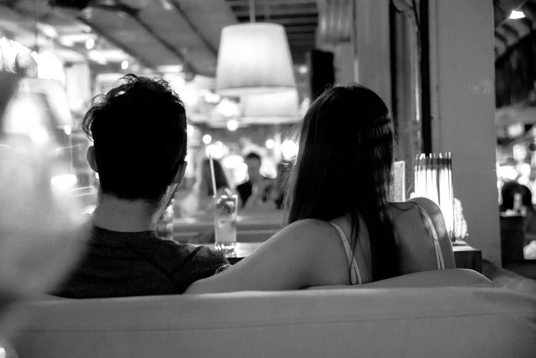 Black-and-white photo of two people on a sofa seen from behind, like a household choosing between IPTV providers such as NEWDYTV